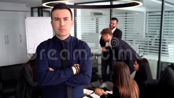 自信的年轻人抱着双臂站在桌子旁背景是会说话的同事视频的预览图