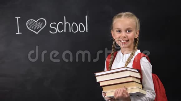 微笑的女学生拿着书我爱写在黑板上的学校课视频的预览图