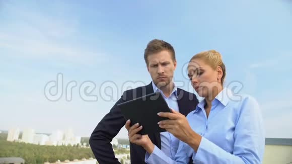 男性和女性员工在户外滚动平板电脑应用程序准备演示文稿视频的预览图