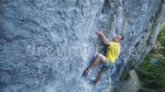穿黄色t恤的攀岩者在悬崖上攀爬寻找到达抓住视频的预览图