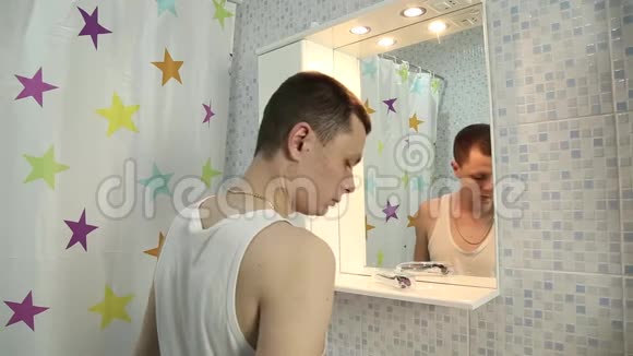 一个年轻有魅力的男人在旅馆房间的浴室里检查他头上的秃顶他经营脱发霜视频的预览图