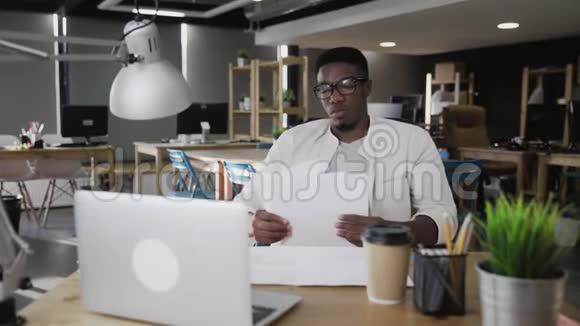 戴眼镜的非洲年轻人坐在办公桌旁看文件视频的预览图