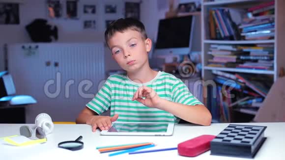 一个男孩坐在课桌旁用手指在平板电脑屏幕上摩擦视频的预览图