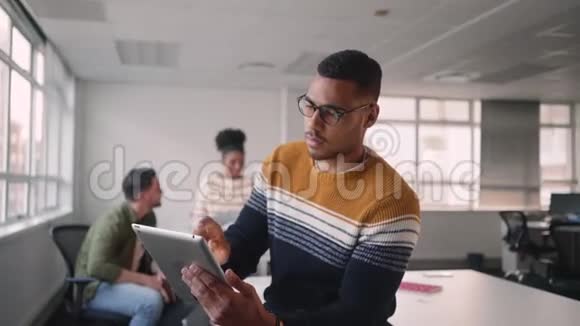 富有创造力的年轻非洲商人忙于使用数字平板电脑他的团队同事在后台讨论工作视频的预览图
