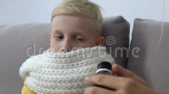 爱心妈妈给咳嗽糖浆生病的男孩子戴围巾喉咙痛治疗视频的预览图