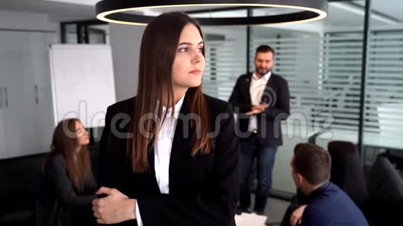 在镜头前的女商人她双臂交叉站在同事面前他们坐在桌子旁视频的预览图