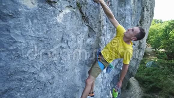 穿黄色t恤的攀岩者在悬崖上攀爬寻找到达抓住视频的预览图