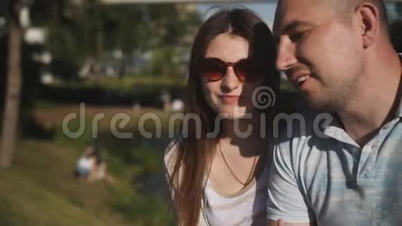 坐在公园长凳上谈情说爱的幸福年轻夫妇视频的预览图
