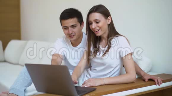 一对夫妇坐在柔软的沙发上在明亮的客厅里看着笔记本电脑视频的预览图