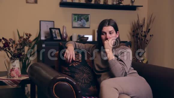 一个穿着棕色西装的欧洲年轻怀孕女孩坐在家里的扶手椅上用手指抠鼻子视频的预览图