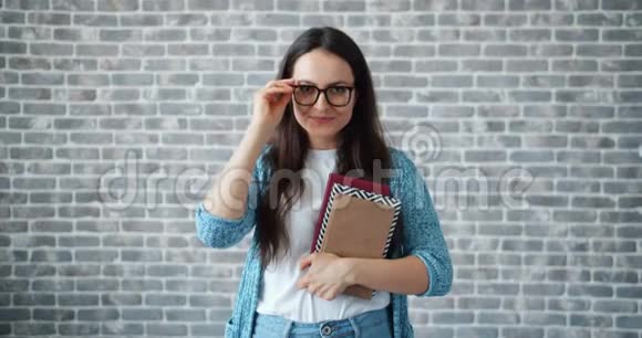 在砖墙背景上戴眼镜拿书的年轻女子视频的预览图