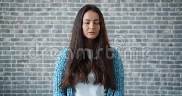 悲伤的年轻女子环顾四周然后在砖块背景上看镜头的画像视频的预览图