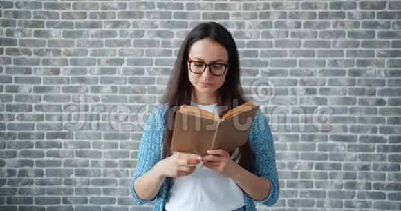 戴眼镜的严肃女孩看书翻页砖墙背景视频的预览图