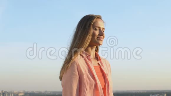 美丽的金发女孩微笑着在城市景观背景上抚摸着头发慢动作视频的预览图