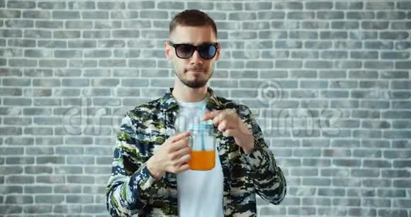 男人喝橙汁然后举起太阳眼镜微笑着站在砖块背景上视频的预览图