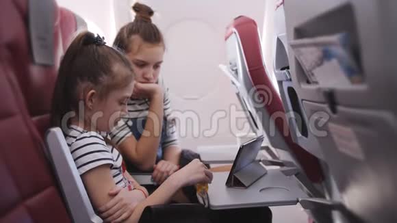 两个姐妹在机舱里飞行时在平板上看动画片视频的预览图