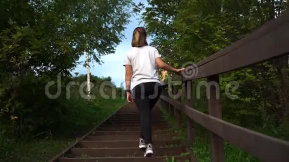 年轻漂亮的运动女孩穿着白色T恤穿着黑色运动裤跑上楼梯慢动作视频的预览图
