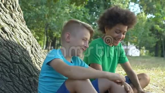 快乐的男孩坐在公园的树下一起玩童年视频的预览图