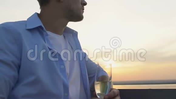 成功的男人拿着一杯白葡萄酒从阳台欣赏美丽的日落视频的预览图