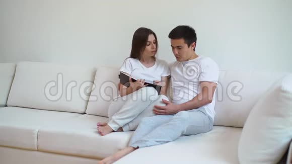 漂亮的一对夫妇坐在白色沙发上在客厅里讨论他们的计划视频的预览图