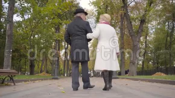 在秋天公园散步的一对高加索族夫妇的后景穿黑衣服的成熟男人穿白衣服的妻子视频的预览图