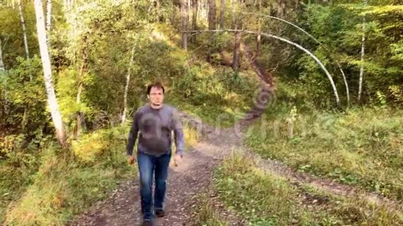 阳光明媚的一天穿牛仔裤的人在公园的小路上散步秋林路景观视频的预览图