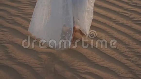 一个穿着白色连衣裙的女人赤脚走在沙漠的沙滩上慢动作视频的预览图