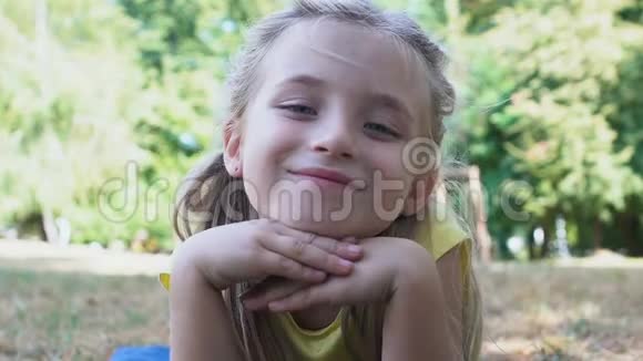 可爱的微笑女孩看着相机躺在公园草夏天休闲童年视频的预览图