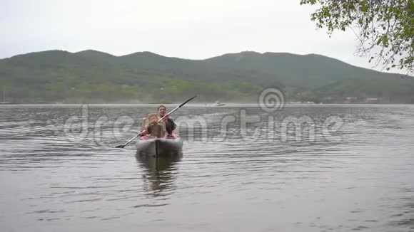 年轻人和他的儿子在海湾或湖边的充气皮艇上划桨慢镜头视频的预览图