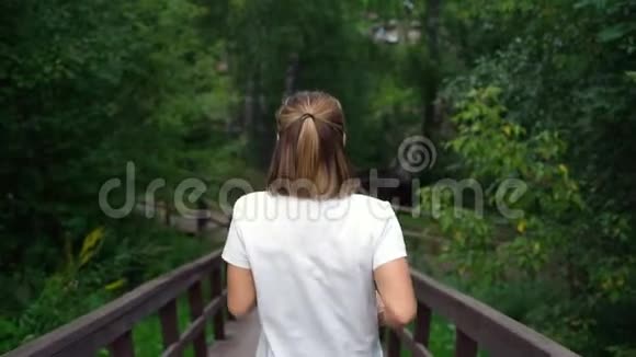 苗条的女孩从公园的楼梯上跑下来穿着白色t恤和黑色运动裤的年轻漂亮的女孩或女人视频的预览图