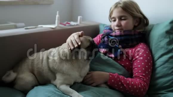生病的小美丽的女孩带着围巾和她的狗在床上女孩身边有药品喷鼻剂视频的预览图