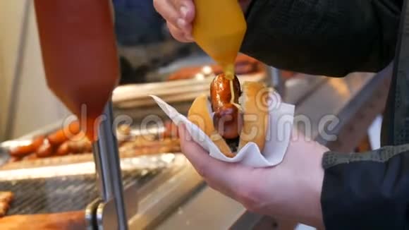 热狗街头垃圾食品雄手拿着一根腊肠用芥末倒在特制的容器里视频的预览图