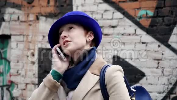 时尚人士戴着蓝色帽子近距离说话电话背景街头涂鸦4K视频的预览图