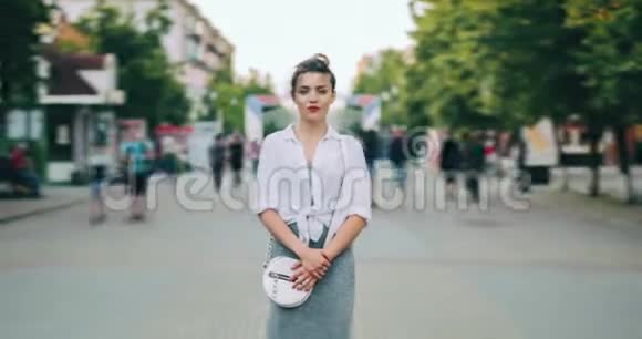 一个漂亮的年轻女士独自站在街上看着摄像机视频的预览图