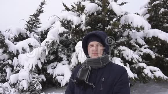 一个年轻英俊的白种人穿着夹克和围巾在冬天的冷杉树的背景下拍摄的视频肖像视频的预览图