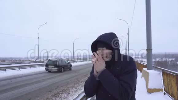 一个年轻的白种人在冬天寒冷的天气里以开车的道路为背景搓手视频的预览图