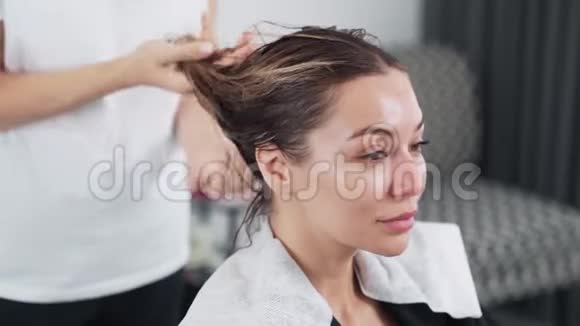 美容师将护理产品应用于美容店年轻女性的湿发视频的预览图