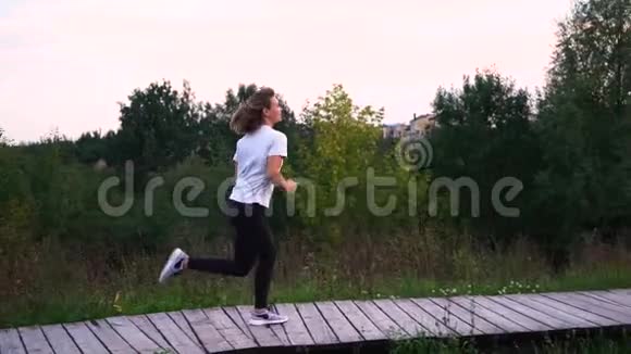 慢动作年轻冷杉苗条女孩或穿白色t恤和黑色运动裤的女人在公园慢动作跑步视频的预览图