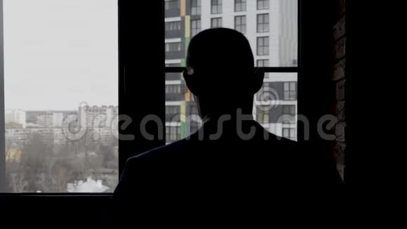 一个穿夹克的人站在窗前从后面看到的视频的预览图