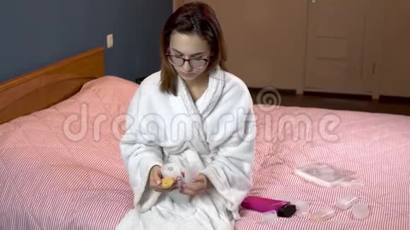 一个女人把洗发水倒进一个小罐子里穿着浴袍的女人拿着一罐旅行洗发水特写视频的预览图