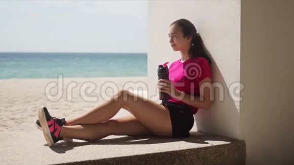 性感的女人带着一瓶水海滩上锻炼后放松视频的预览图