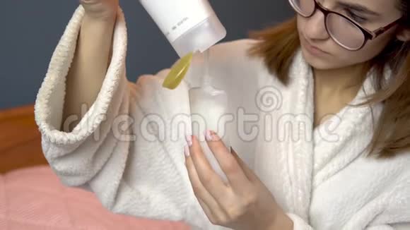 一个女人把洗发水倒进一个小罐子里穿着浴袍的女人拿着一罐旅行洗发水特写视频的预览图