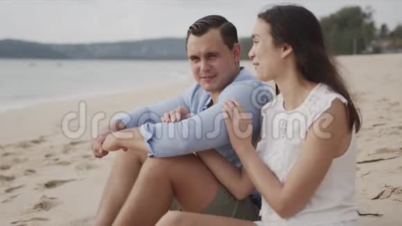 一对在海边坐在沙滩上微笑着度假的夫妇视频的预览图