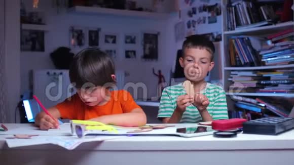两个学生坐在桌子旁一个写着第二个玩着视频的预览图