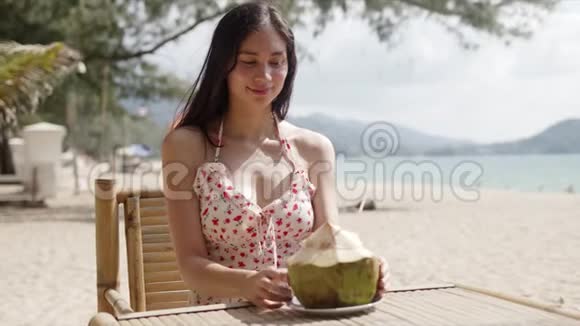 年轻女子坐在桌上沙滩上放着椰子视频的预览图