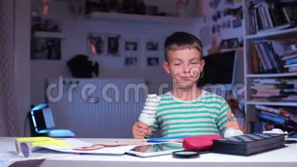 男孩坐在一张桌子旁展示灯泡表现得像视频的预览图