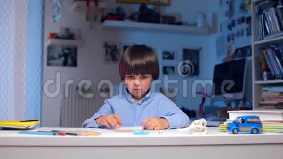 一个男孩坐在桌子旁看着相机翻阅着一本书视频的预览图