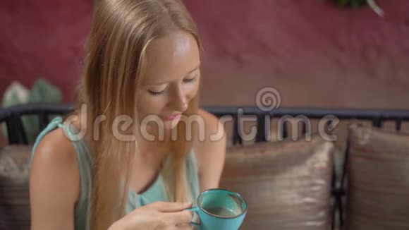 年轻女子坐在漂亮的咖啡馆里享受蓝色拿铁热蝶豌豆拿铁或蓝色螺旋藻拿铁慢动作视频的预览图