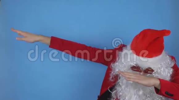 一个留着胡须穿着圣诞老人服装的年轻人在蓝色背景下在度假时表现出一种现代的姿态视频的预览图