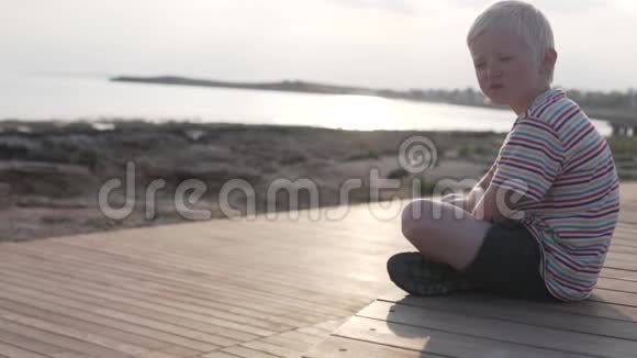 一个悲伤的男孩坐在海边的水边视频的预览图